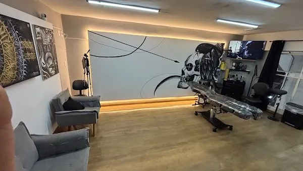 Sala de tatuagem com maca preta, poltronas cinza e um grande painel de caveira na parede